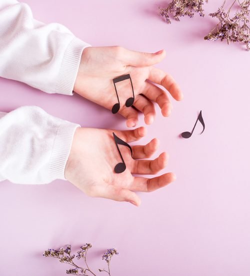 Children's hands hold paper notes on a pink background. Music ed